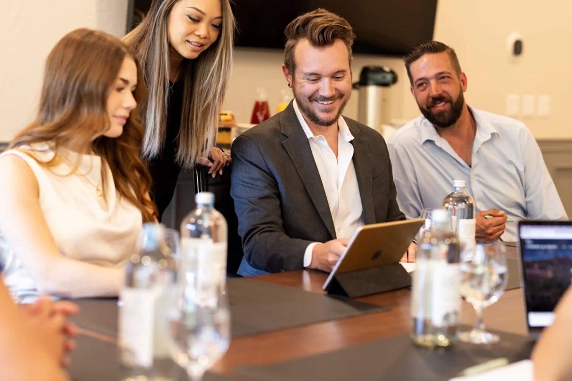 A close-up of professionals in a meeting, smiling and looking at a tablet on the conference table.